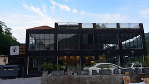 A modern building with large windows, a sign for La Orilla Hotel & Restaurant, and a parking area with a car. - La Orilla Hotel (Muzaffarabad)
