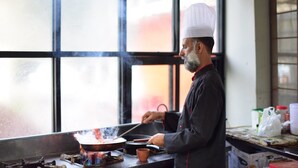 A chef cooking in a kitchen with a large window, a stove, and cooking utensils. - La Orilla Hotel (Muzaffarabad)