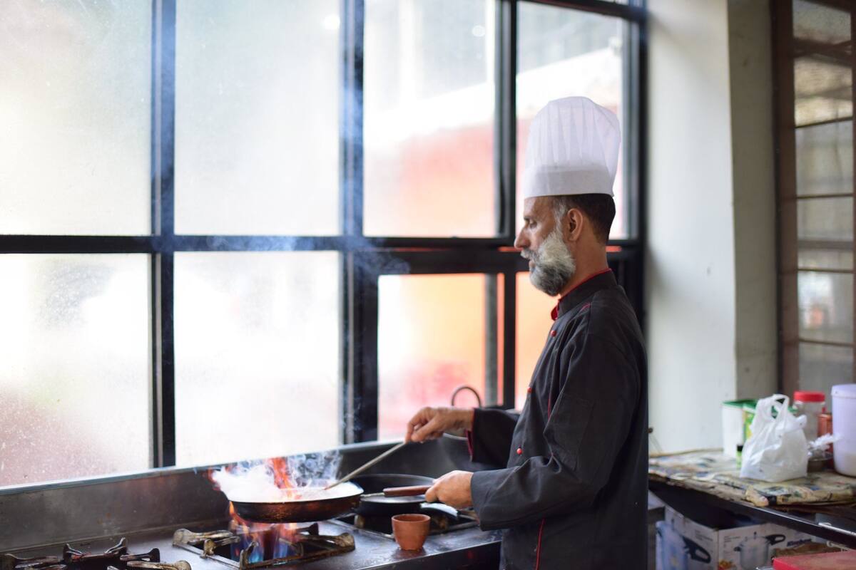 Un chef cuisinant dans une cuisine dotée d’une grande fenêtre, d’une cuisinière et d’ustensiles de cuisine.