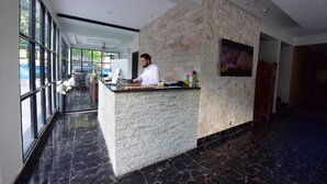 A reception area with a stone counter, a computer, and a TV on the wall. - La Orilla Hotel (Muzaffarabad)