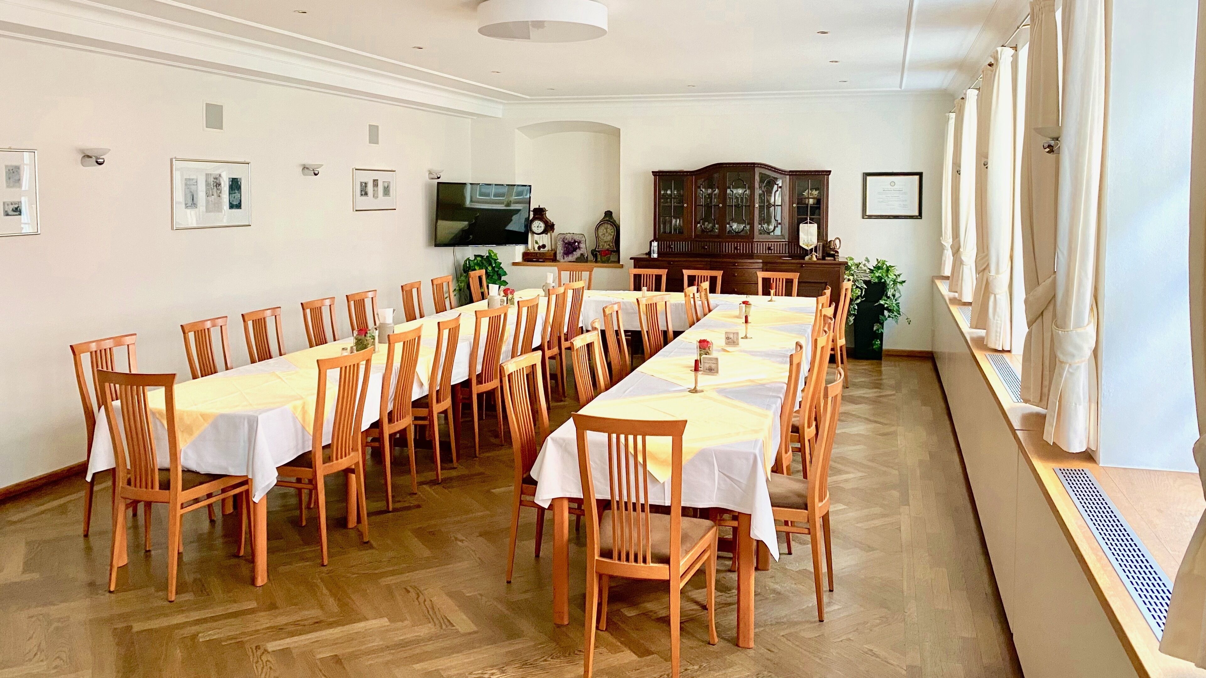 Un comedor con mesas largas y sillas de madera, un televisor y cuadros en las paredes.