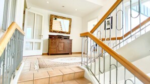 Una escalera con barandilla de madera y balaustrada de cristal, que conduce a un rellano con un espejo grande y un armario de madera.