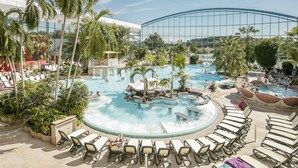 Zona de piscina en un resort, con varias piscinas, sillas de descanso y palmeras.
