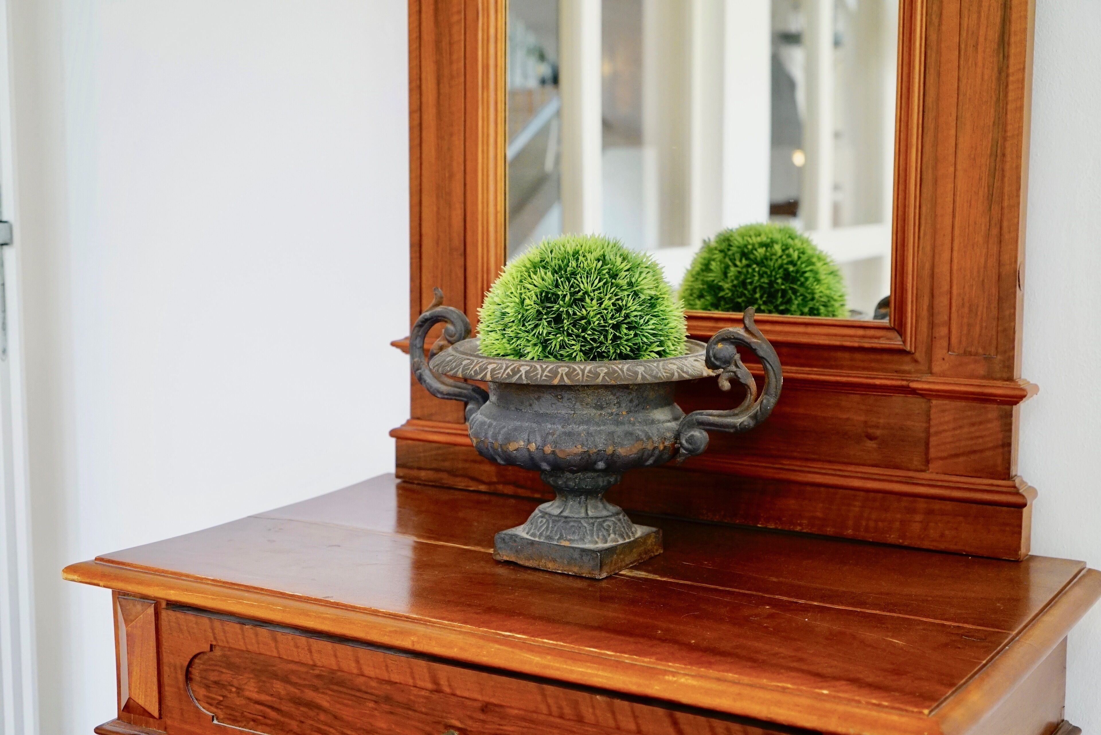 A wooden dresser with a decorative urn containing a spherical green plant.