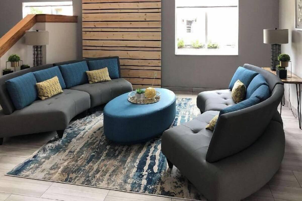 A modern living room with a sectional sofa, a round ottoman, and a patterned rug.