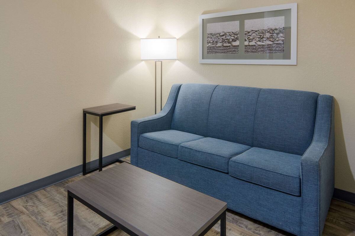 A room with a blue sofa, a small table, a floor lamp, and a framed picture on the wall.