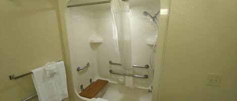 A bathroom with a bathtub, a shower, and a wooden shelf.