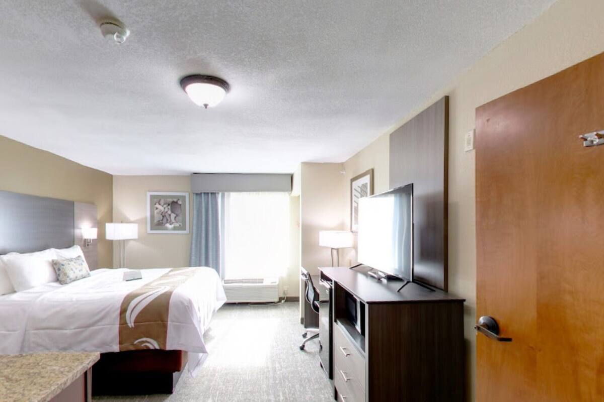 A hotel room with a bed, bedside tables, a desk, a TV, and a wooden door.