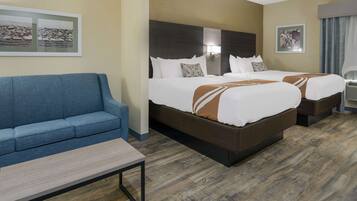 A hotel room with two beds, a blue sofa, a small table, and artwork on the walls.