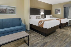 A hotel room with two beds, a blue sofa, a small table, and artwork on the walls.