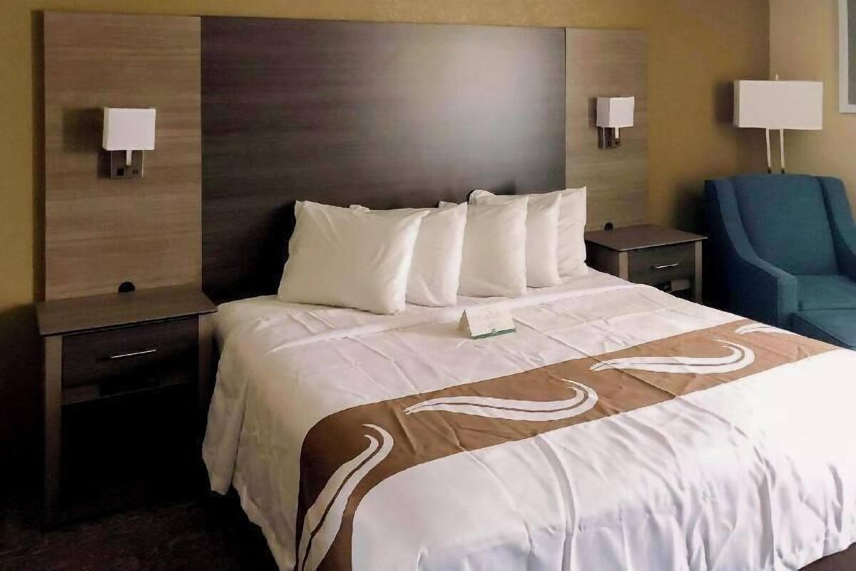 A hotel room with a large bed, two bedside tables, a chair, and wall-mounted lamps.