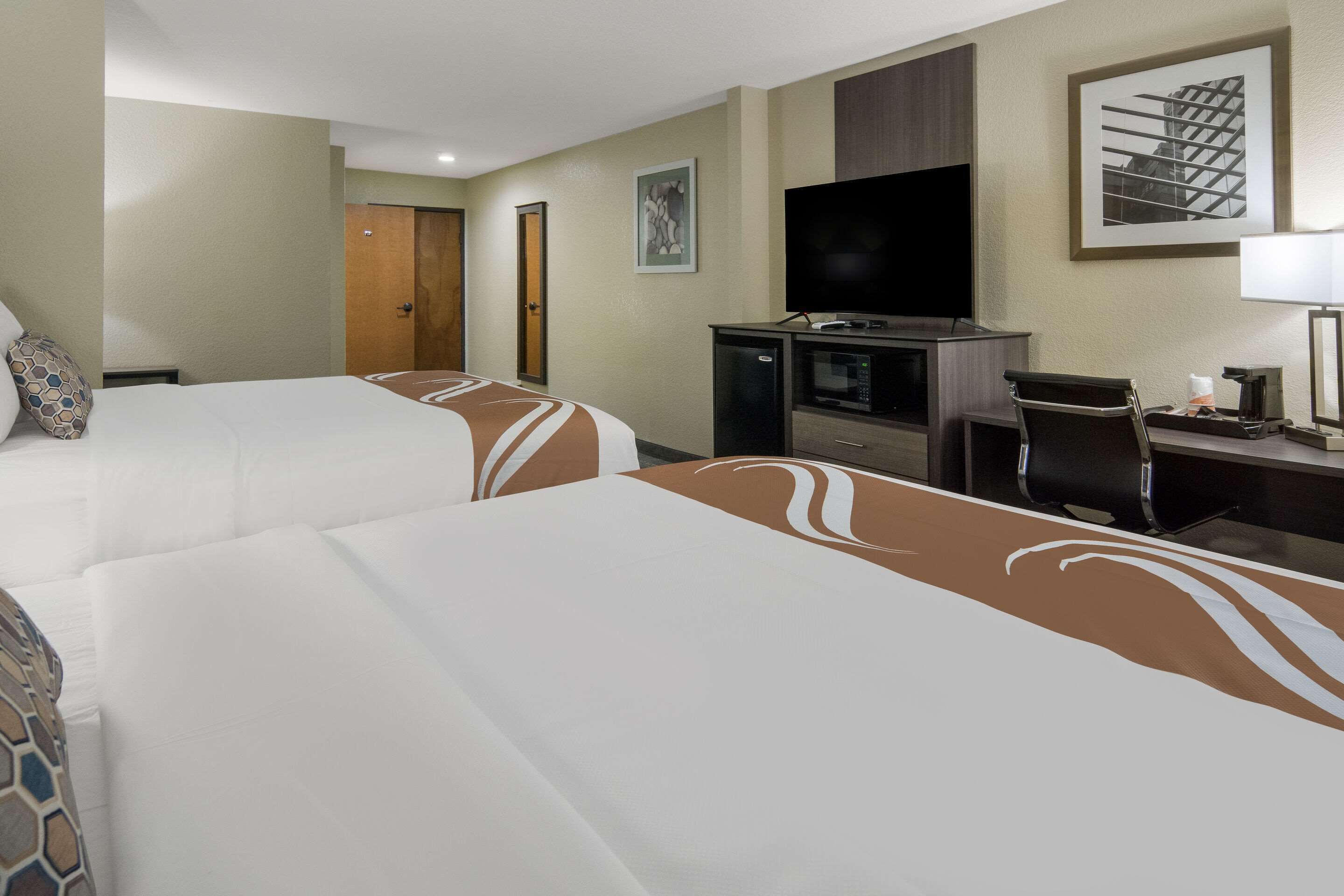 A hotel room with two beds, a TV, a desk, and a microwave.