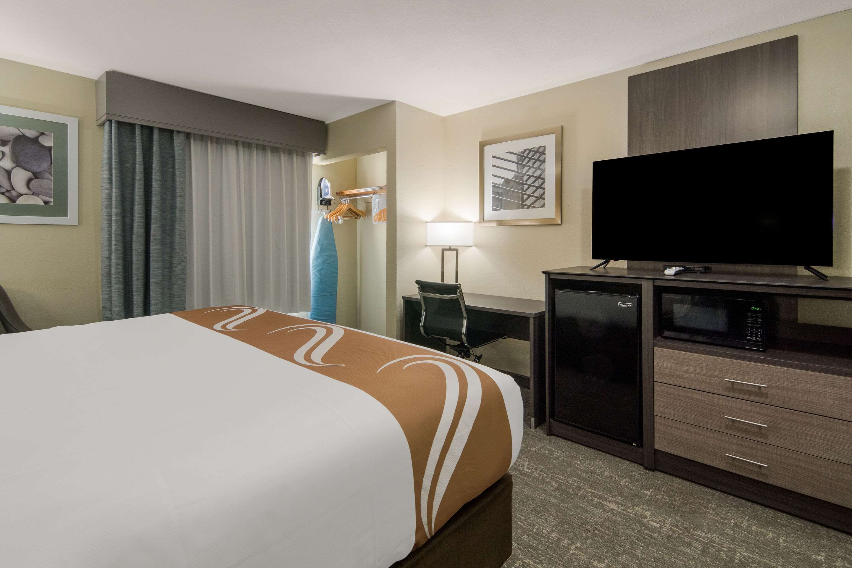Una habitación de hotel con una cama, un escritorio, un televisor, un microondas y un refrigerador.