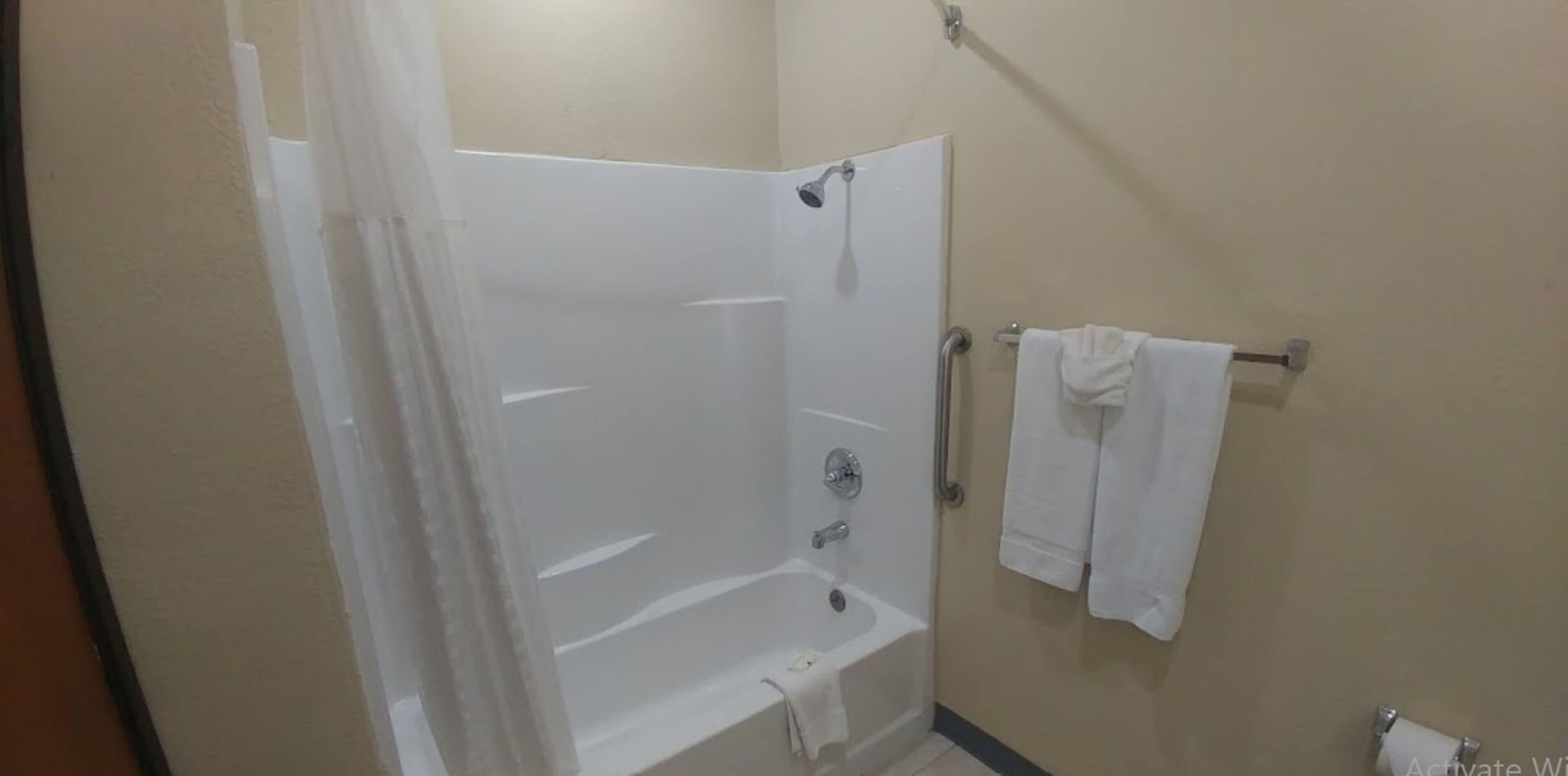 A bathroom with a shower, a bathtub, and a towel rack with towels.