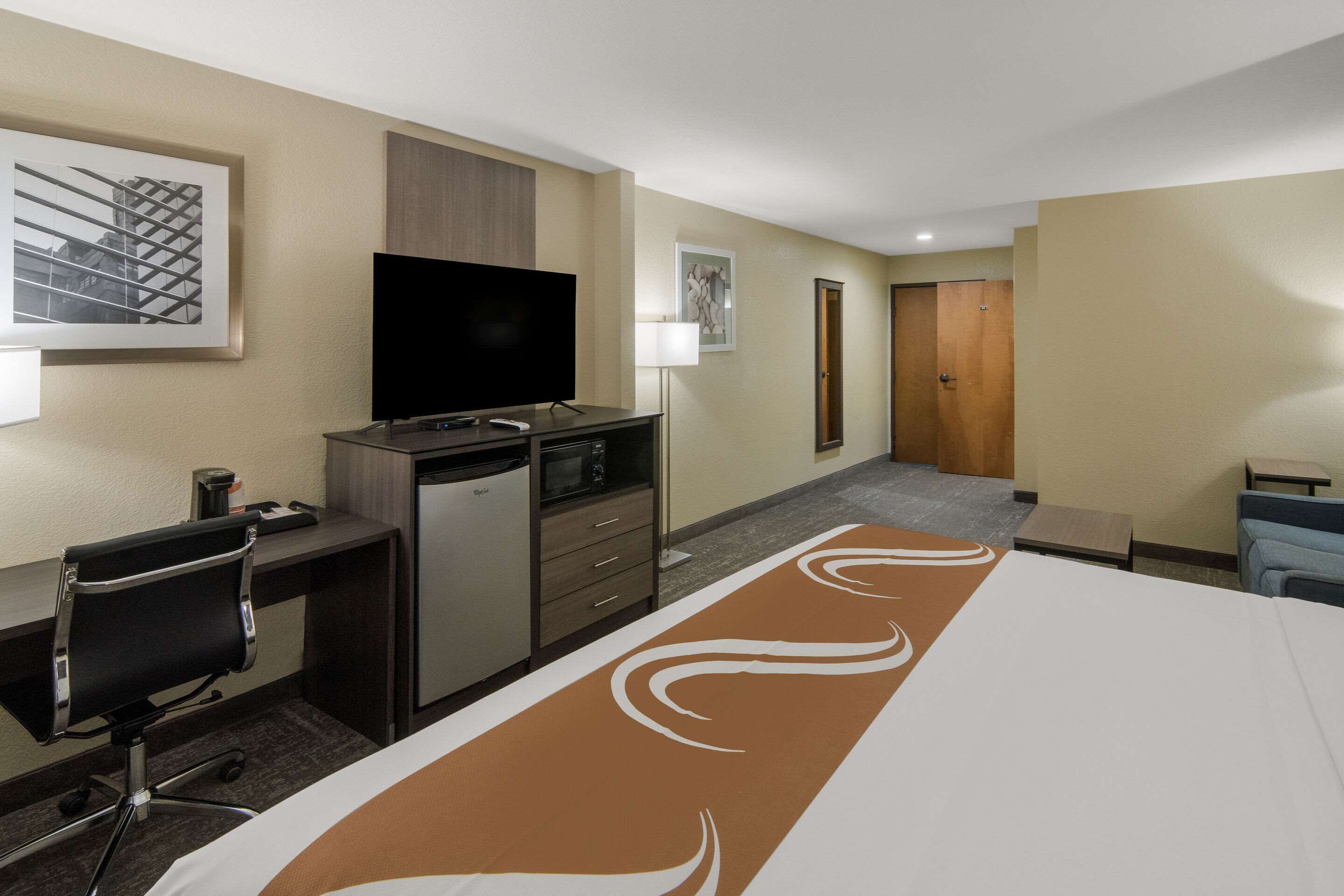 A hotel room with a bed, desk, chair, television, microwave, and a door leading to another room.