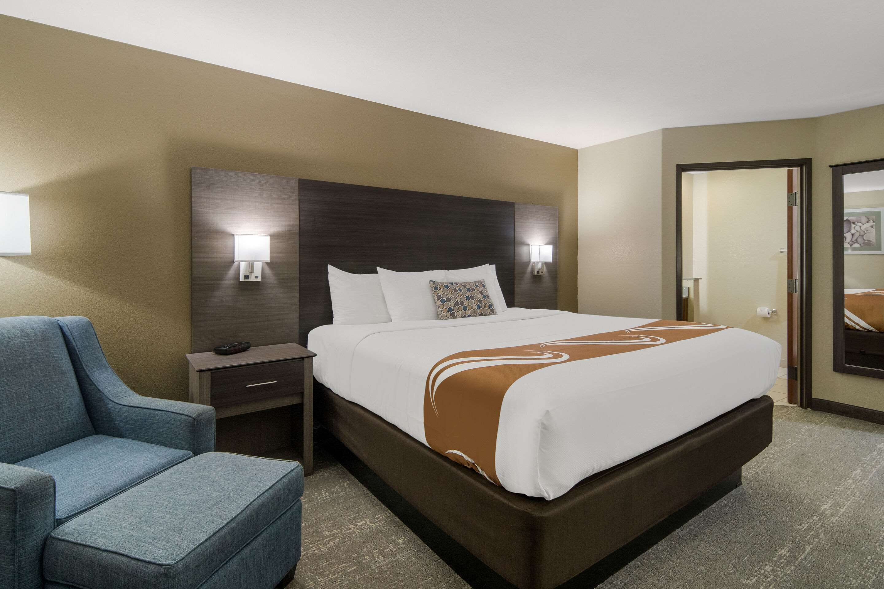 Ein Hotelzimmer mit einem großen Bett, einem Nachttisch, einem Sessel und einem Spiegel.