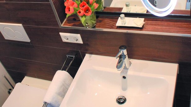 Un baño con lavamanos blanco, inodoro, bidé, espejo con luz y un jarrón con flores.