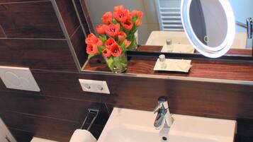 Ein Badezimmer mit einem weißen Waschbecken, einer Toilette, einem Bidet, einem Spiegel mit Beleuchtung und einer Vase mit Blumen.