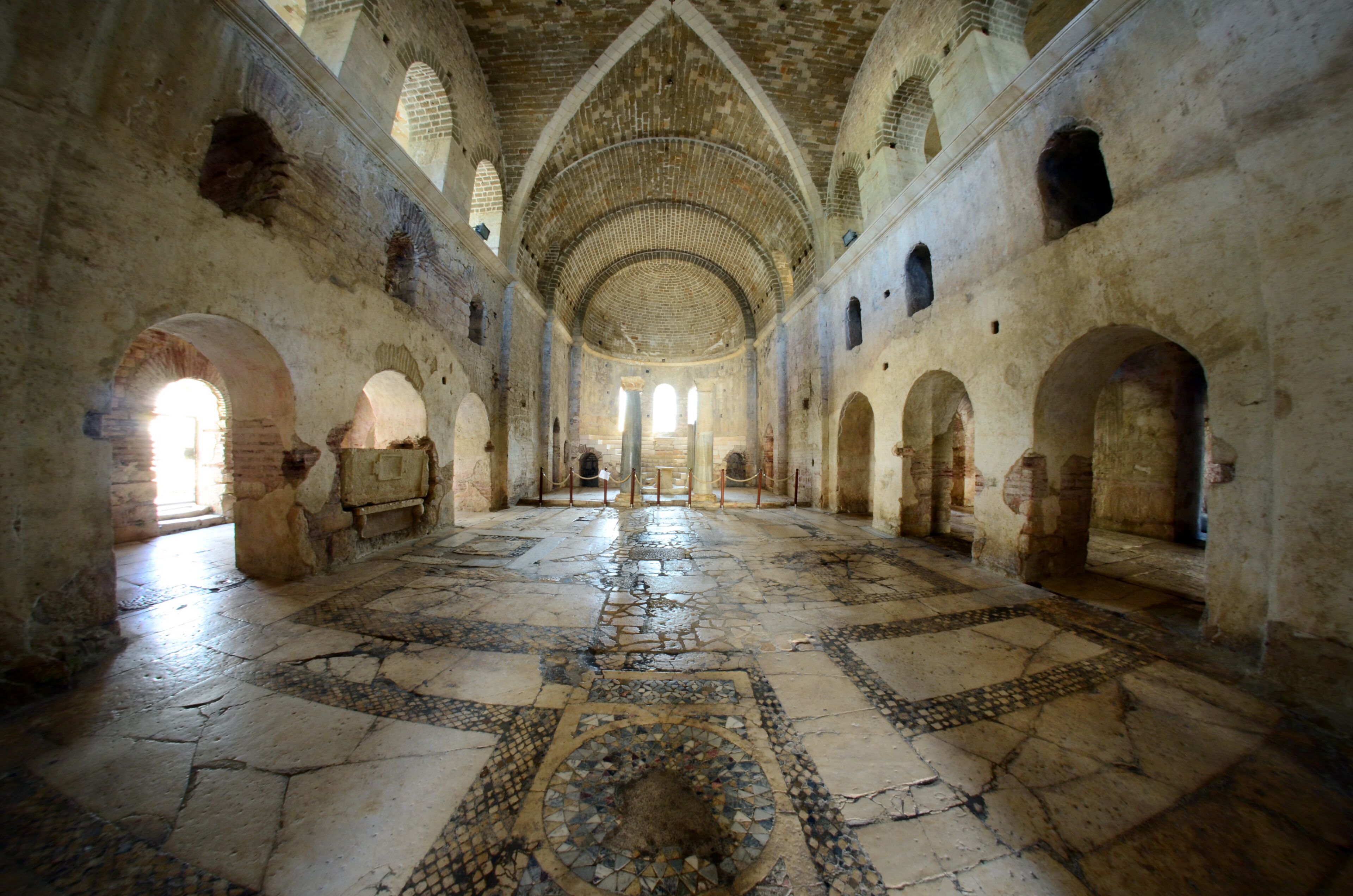 An interior with arched ceilings, a patterned floor, and stone walls.
