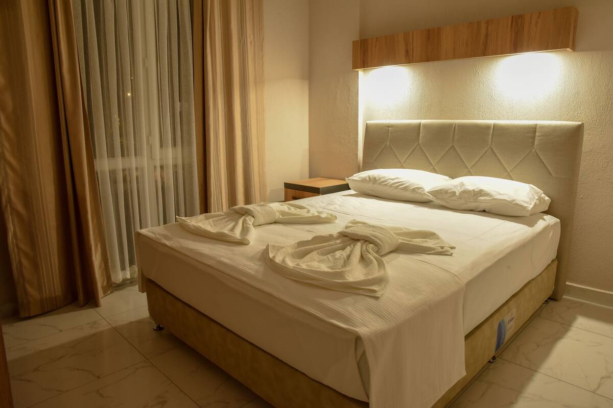 A neatly made bed with a headboard, a bedside table, and a curtain.