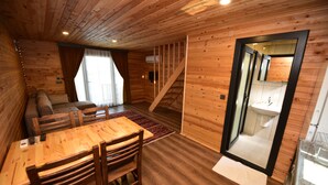 A wooden cabin interior with a dining area, sofa, staircase, and a bathroom visible through a glass door. - Irbec Apart & Bungalow (Demre)