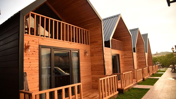 A row of wooden cabins with balconies, large sliding glass doors, and a paved patio area. - Irbec Apart & Bungalow (Demre)