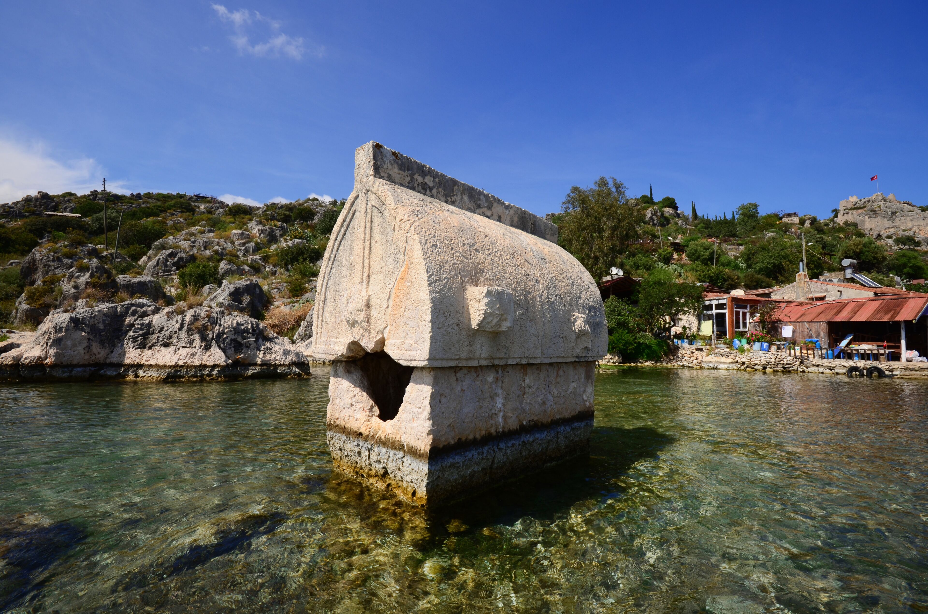 A stone structure in clear water with a rocky hillside in the background.