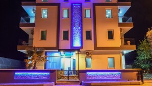 A multi-story building with balconies, a central vertical light feature, and a water feature at the entrance. - Irbec Apart & Bungalow (Demre)