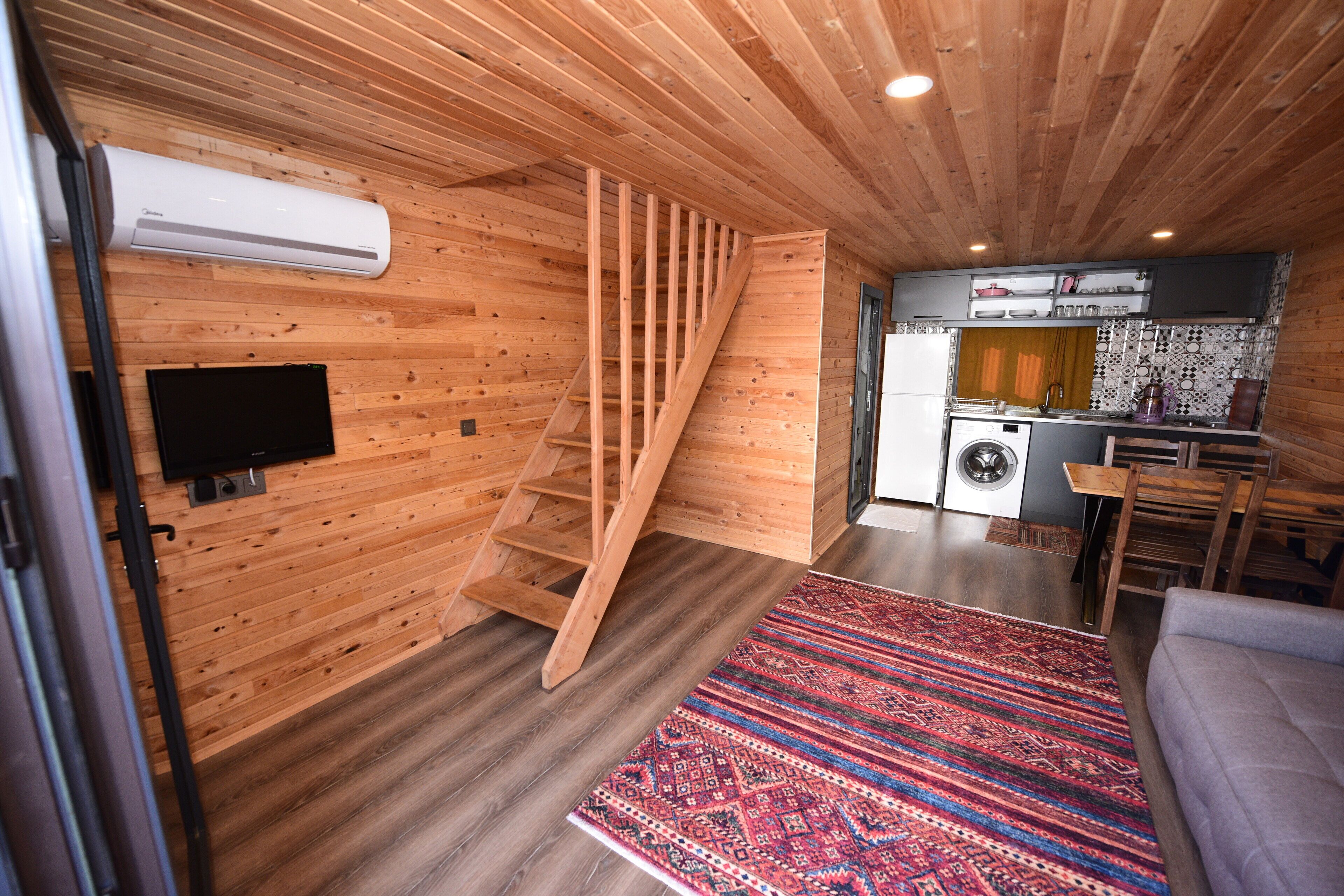 Un interior de madera con una escalera, lavadora y zona de cocina.