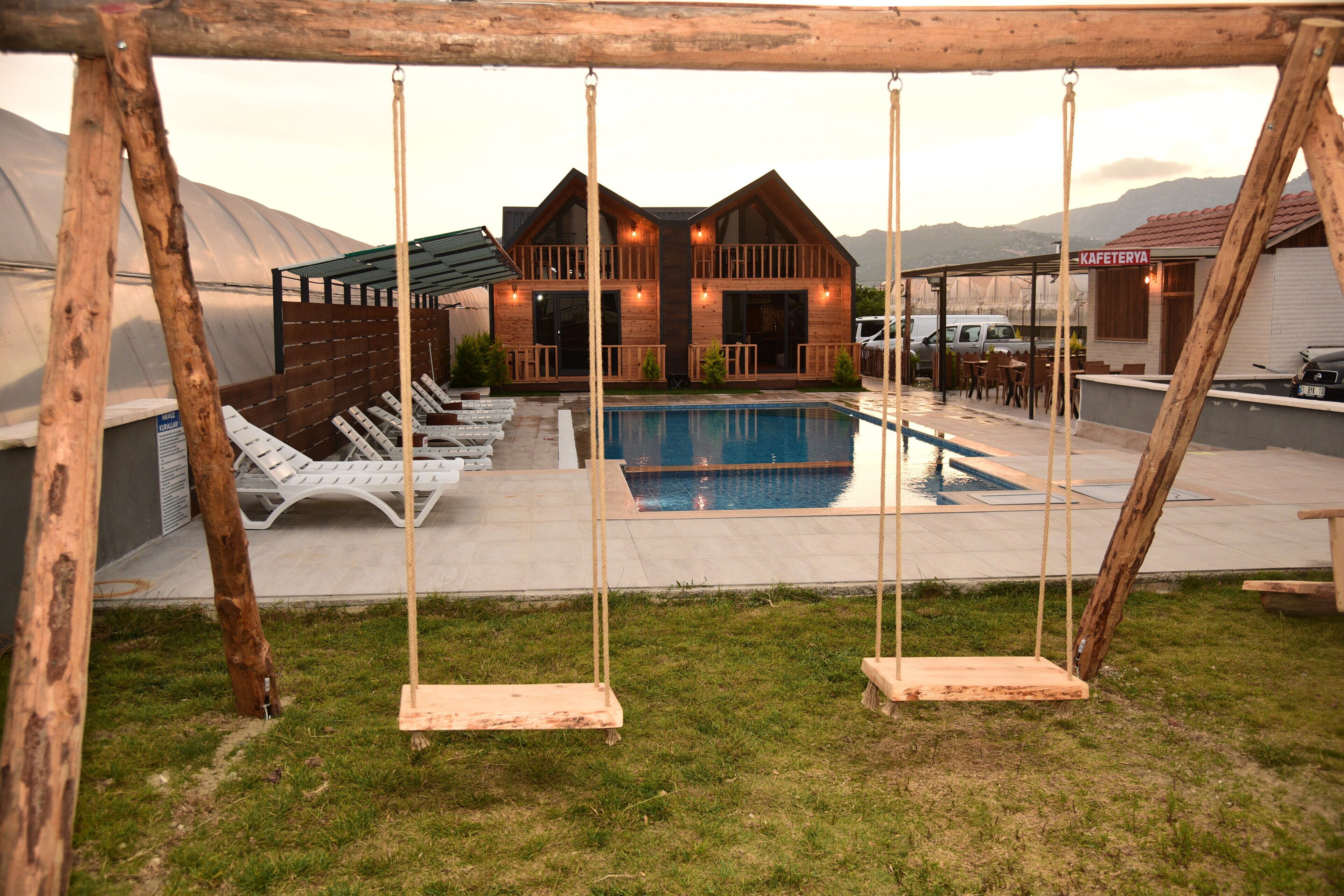 A wooden house with a pool, lounge chairs, and a swing set.