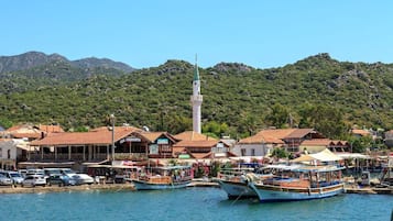 A coastal town with traditional buildings, a prominent tower, and boats docked at the harbor.