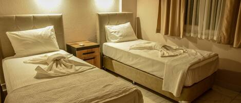 Habitación de hotel con dos camas, una mesita de noche y un ventanal con cortinas.