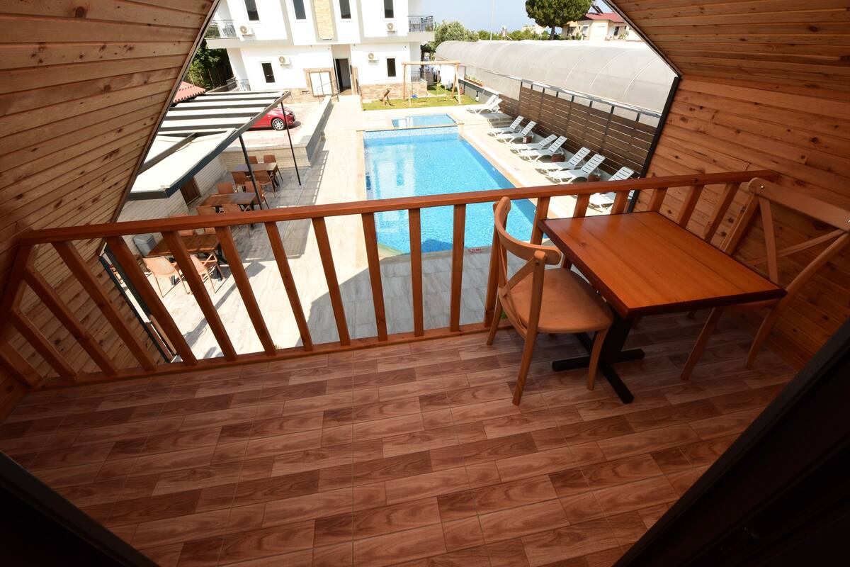 A wooden balcony with a pool view, wooden deck, and a table with chairs.