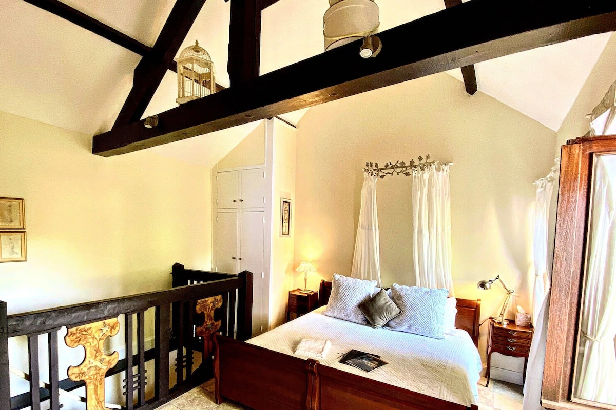 Une chambre à coucher avec un lit en bois, une table de chevet, une commode, une armoire et une fenêtre avec des rideaux.