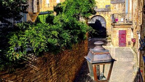 Una estrecha calle adoquinada con edificios antiguos, un muro de piedra y un farol.