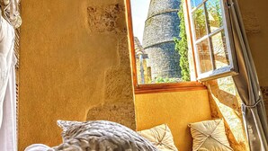 Un dormitorio con un ventanal grande que da a una torre de piedra, una cama con ropa de cama estampada y vistas al exterior.