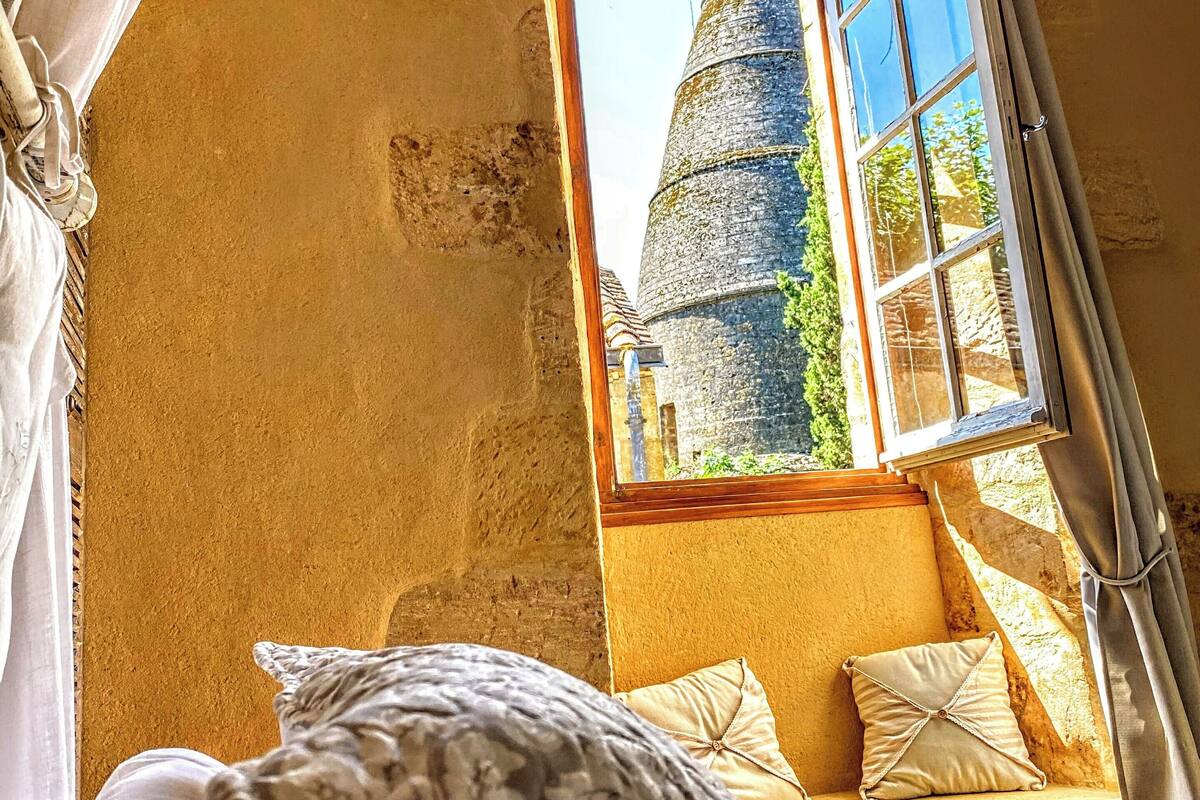 Une chambre avec une grande fenêtre donnant sur une tour en pierre, un lit avec une literie à motifs et une vue sur l’extérieur.