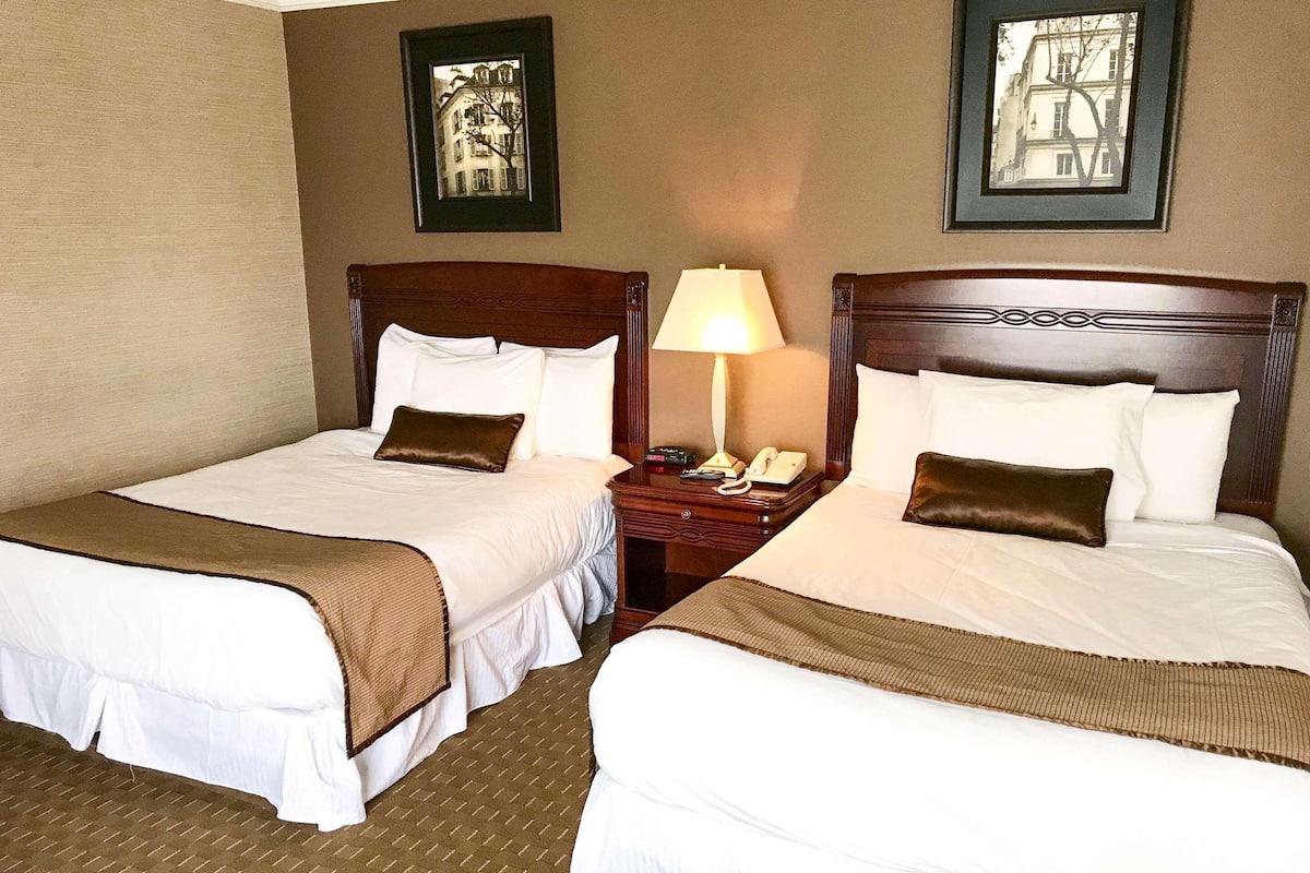 A hotel room with two beds, a nightstand with a lamp, and framed pictures on the wall.