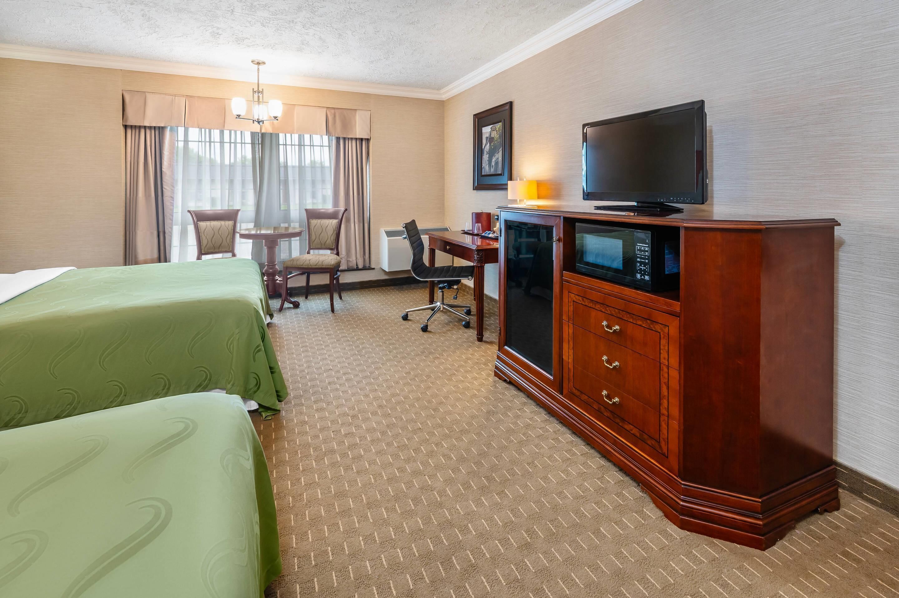 A hotel room with two beds, a desk, a television, and a cabinet.