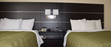 Et hotelværelse med to senge, et natbord og en lampe monteret på væggen.