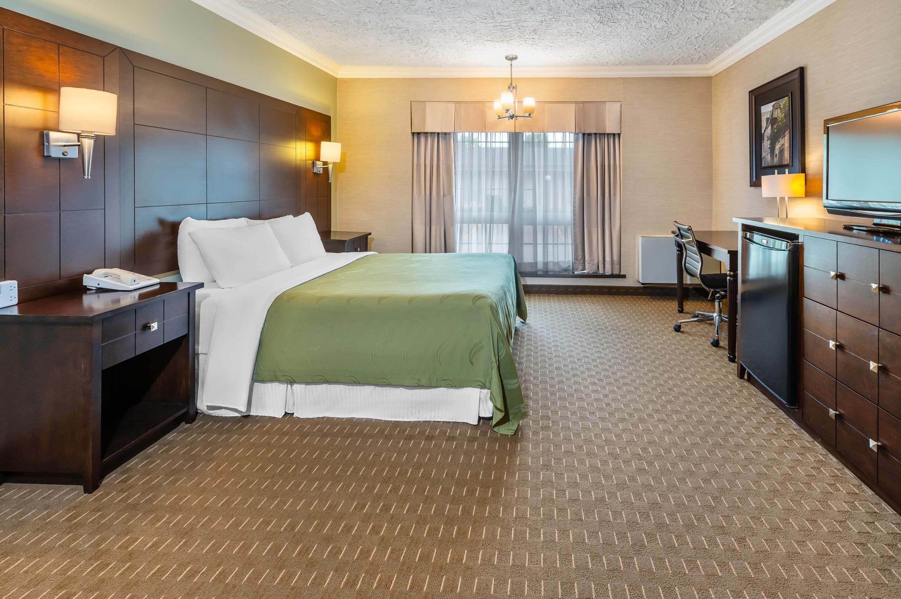 Ein Hotelzimmer mit einem großen Bett, einem Schreibtisch mit Telefon, Fernseher und einer Schreibtischlampe.