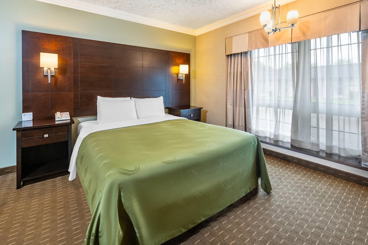 A hotel room with a large bed, two bedside tables, a nightstand, a lamp, and a window with curtains.