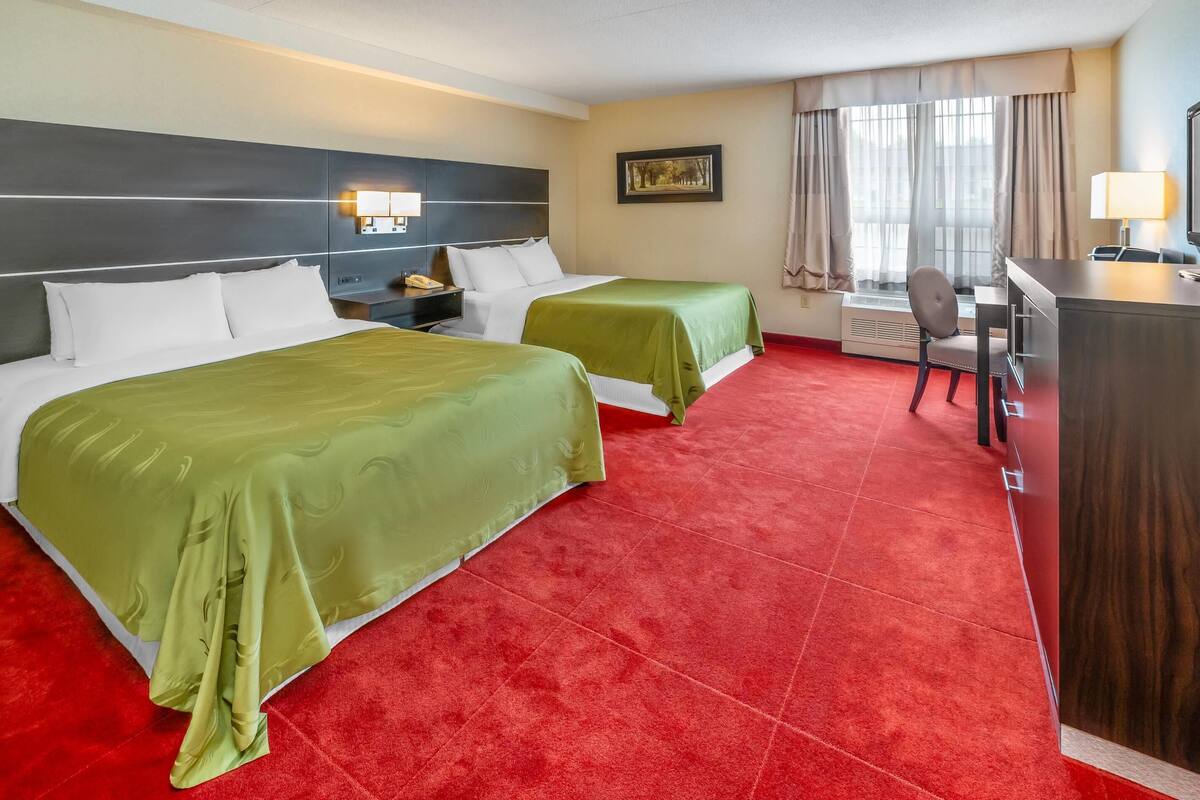 A hotel room with two beds, a desk, a chair, and a window with curtains.