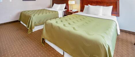 Habitación de hotel con dos camas, cada una con cabecero de madera, una mesita de noche con lámpara y un cuadro en la pared.