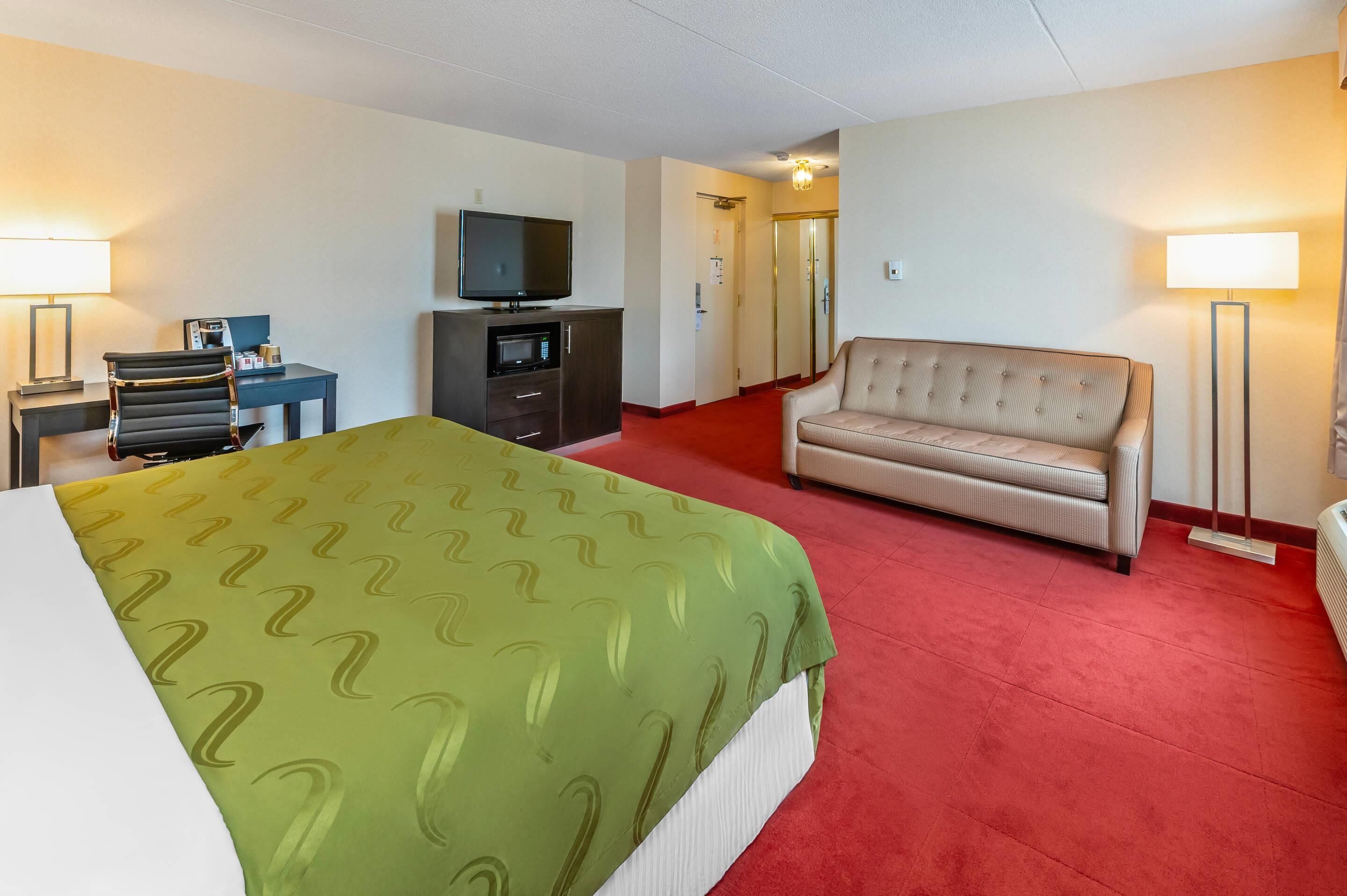 A hotel room with a bed, a sofa, a TV, a desk, and a lamp.