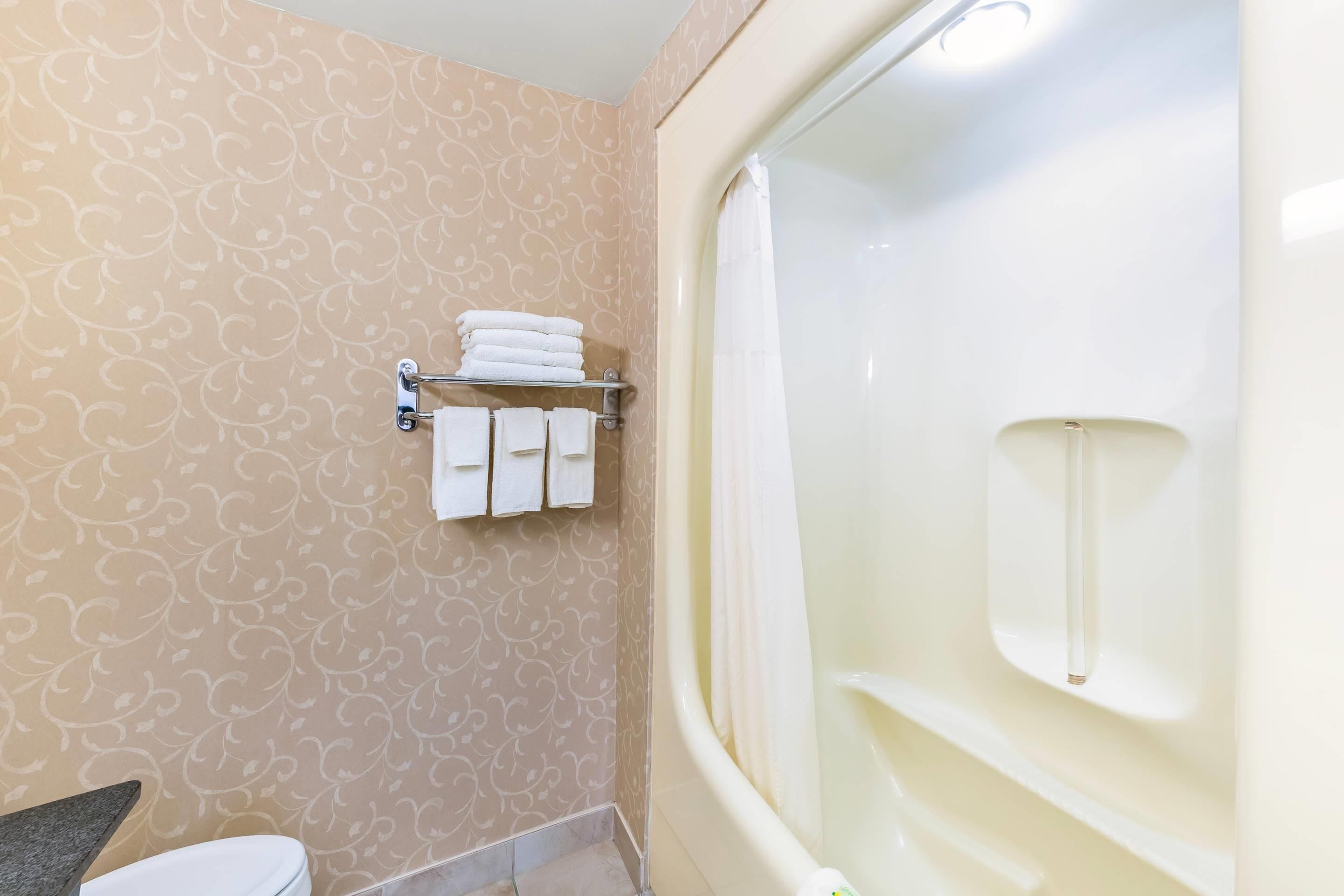 A bathroom with a bathtub, a toilet, and a towel rack with folded towels.