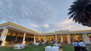 Un salón de banquetes al aire libre con varias mesas redondas dispuestas para cenar, rodeado de un césped bien cuidado.