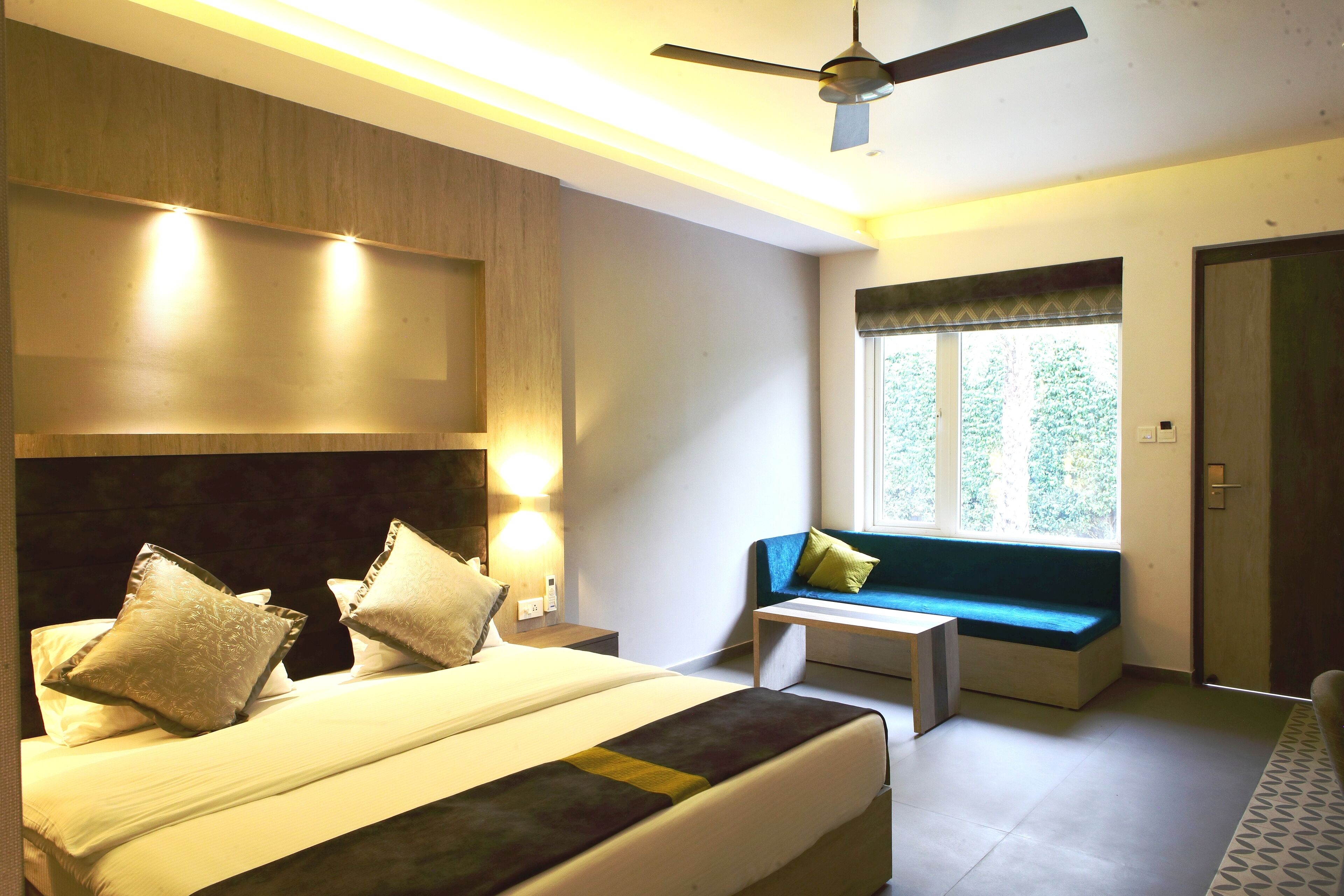 A bedroom with a bed, bedside tables, a ceiling fan, a window with a view, and a door.