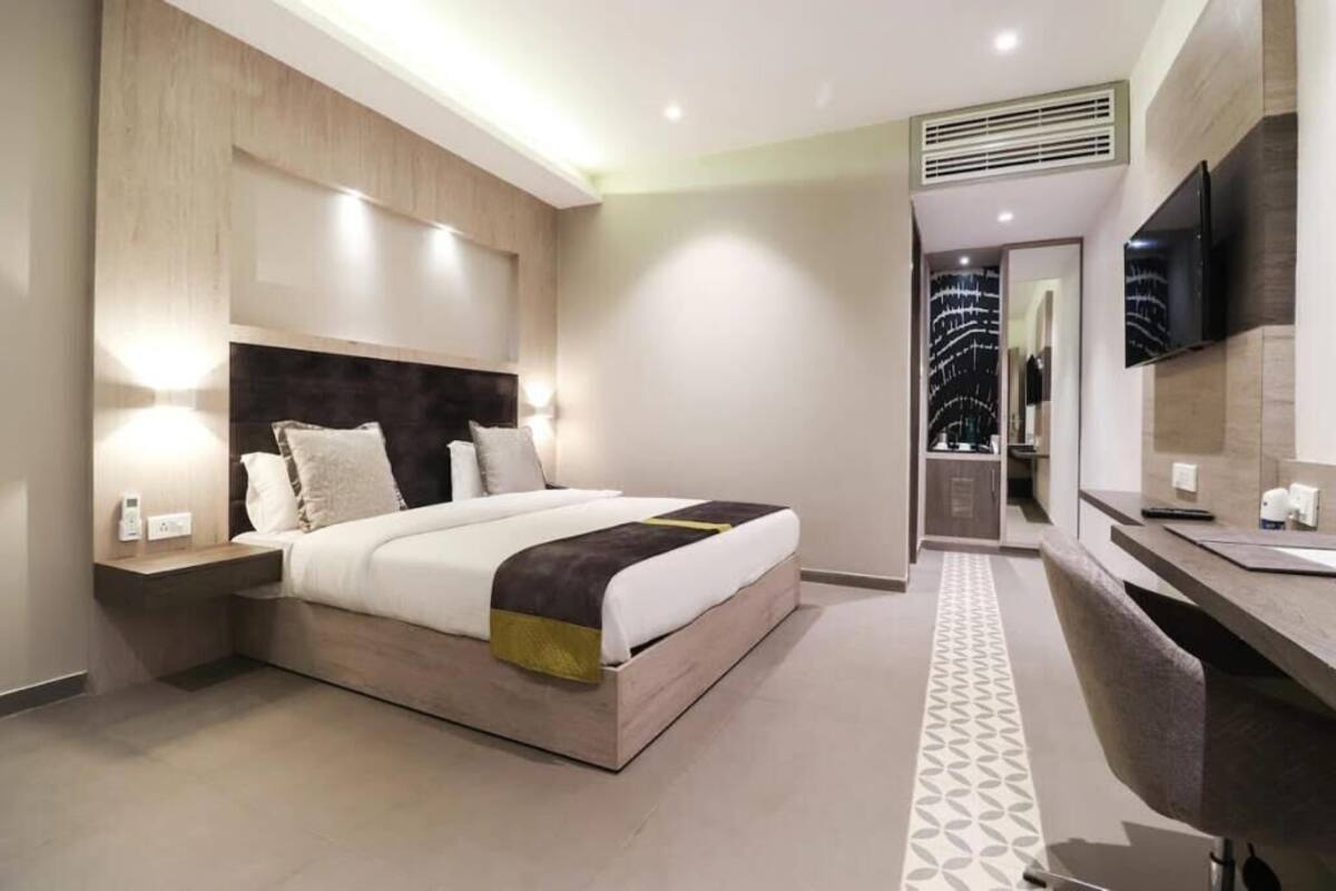 Una habitación de hotel moderna con una cama grande, una mesita de noche y un televisor montado en la pared.