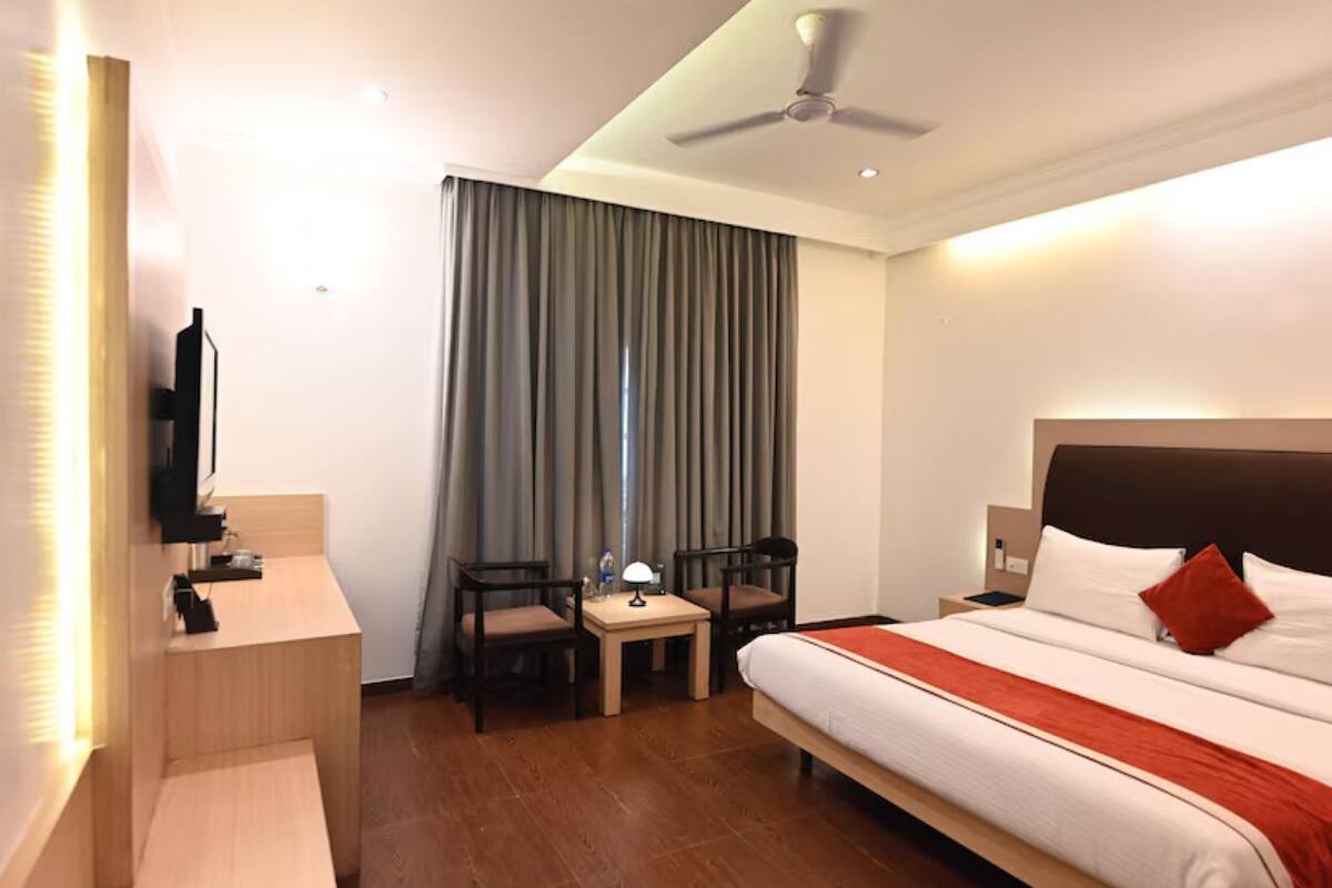 Una habitación de hotel con una cama, un escritorio con silla, un televisor y un ventilador de techo.